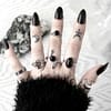 hand with occult finger tattoos and long black nails on white background showing multiple silver rings, from the left - 1 sacred geometry pattern silver ring, 1 pentgram ring in sterling silver, 1 snake ring with black onyx, 1 rutile ring in sterling silver and on the tumb 1 moon ring.