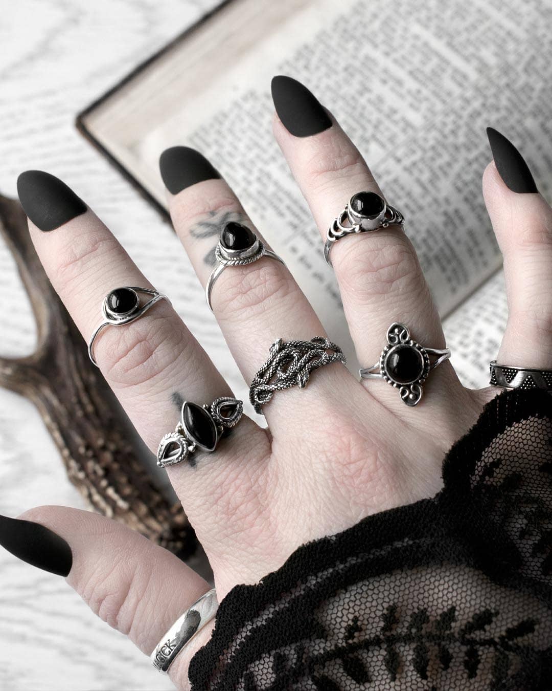 Hand with long black nails, occult finger tattoos, and many sterling silver rings, in the middle a duo snake ring