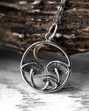 Close-up view of recycled sterling silver necklace with intricate details and oxidised finish, the neckless is 3 mushrooms under a crescent moon, all enframed in a circle, light autumn themed background