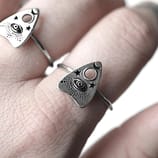Close-up view of fingers with 2 recycled sterling silver rings with Ouija Spirit board detailed symbol, all white background