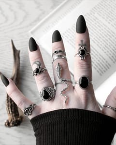 Hand with long black nails, occult finger tattoos, and many sterling silver rings, in the middle a large snake ring - the mother of sepent ring, sourunded by black onyx silver rings