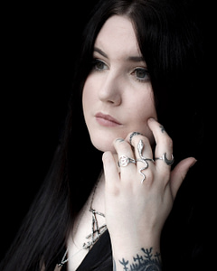 pale goth girl with raven black hair showing sterling silver rings, in the middle the mother of serpent snake ring, paired with sigil of lucifer necklace.
