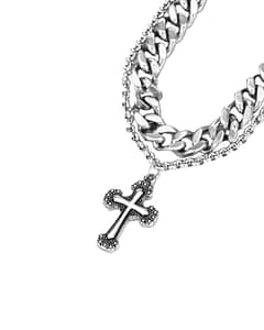 Close-up on a gothic cross pendant with intricate details, hanging in a thin chain together with a bold thick chain. Stainless Steel. Steel grey colour.