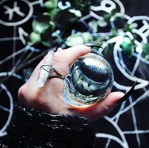 hand with long black nails holding a crystal ball