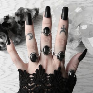 hand with long black nails and oval rutilated quartz rings in sterling silver on white background with crystal clusters