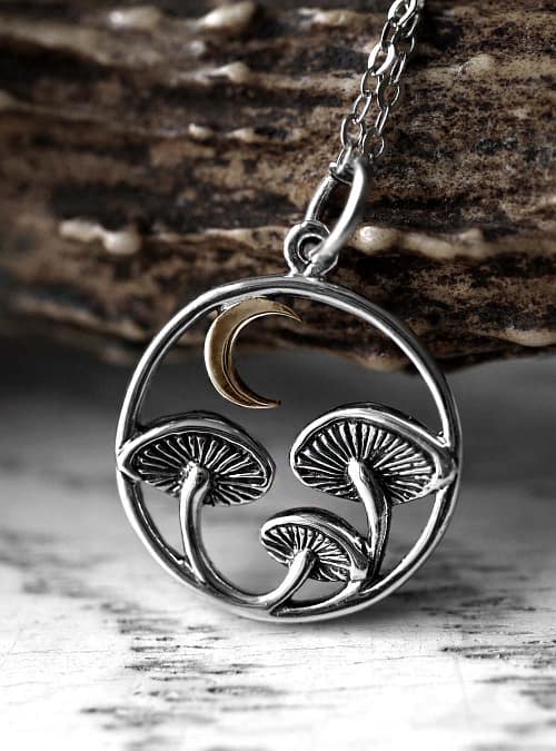 Close-up view of recycled sterling silver necklace with intricate details and oxidised finish, the neckless is 3 mushrooms under a crescent moon, all enframed in a circle, light autumn themed background