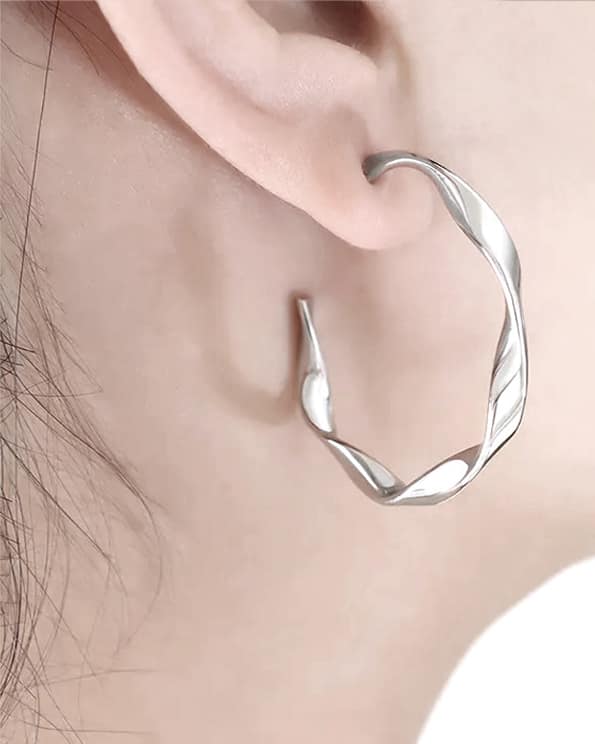 A twisted stainless steel earring hanging in a womans ear.