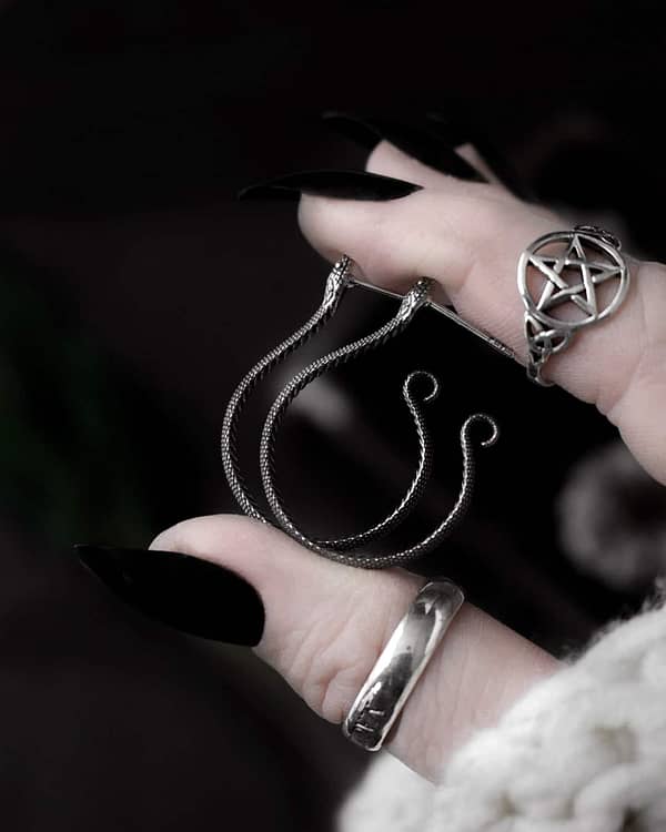 hand holding snake earrings, side view. also showing a pagan pentagram ring in sterling silver.