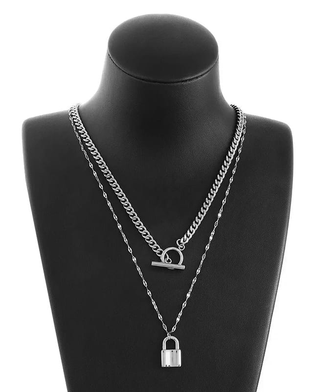 Two chain necklaces hanging on a black necklace bust display. One lock pendant hanging in a thin chain, above it hangs a chunky chain choker in stainless steel. White background