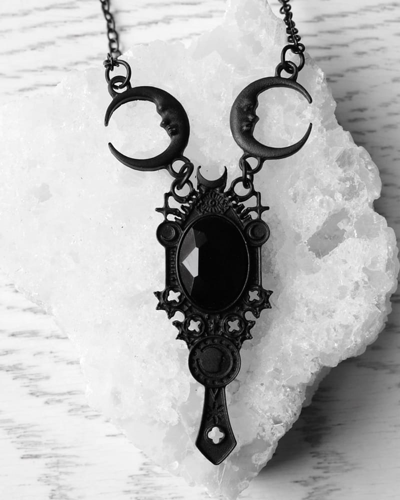 A black necklace laying on a crystal quartz stone. The necklace has a black stone in the middle which is surrounded by a frame with pagan symbols and crescent moons.