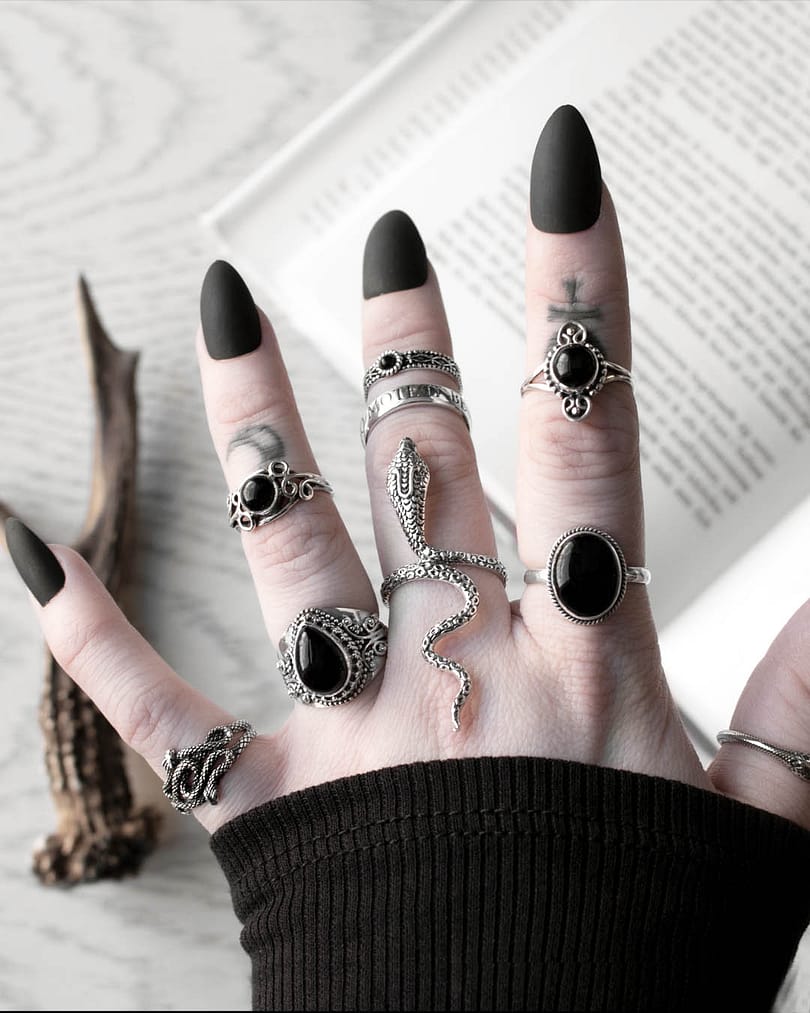 Hand with long black nails, occult finger tattoos, and many sterling silver rings, in the middle a large snake ring - the mother of sepent ring, sourunded by black onyx silver rings