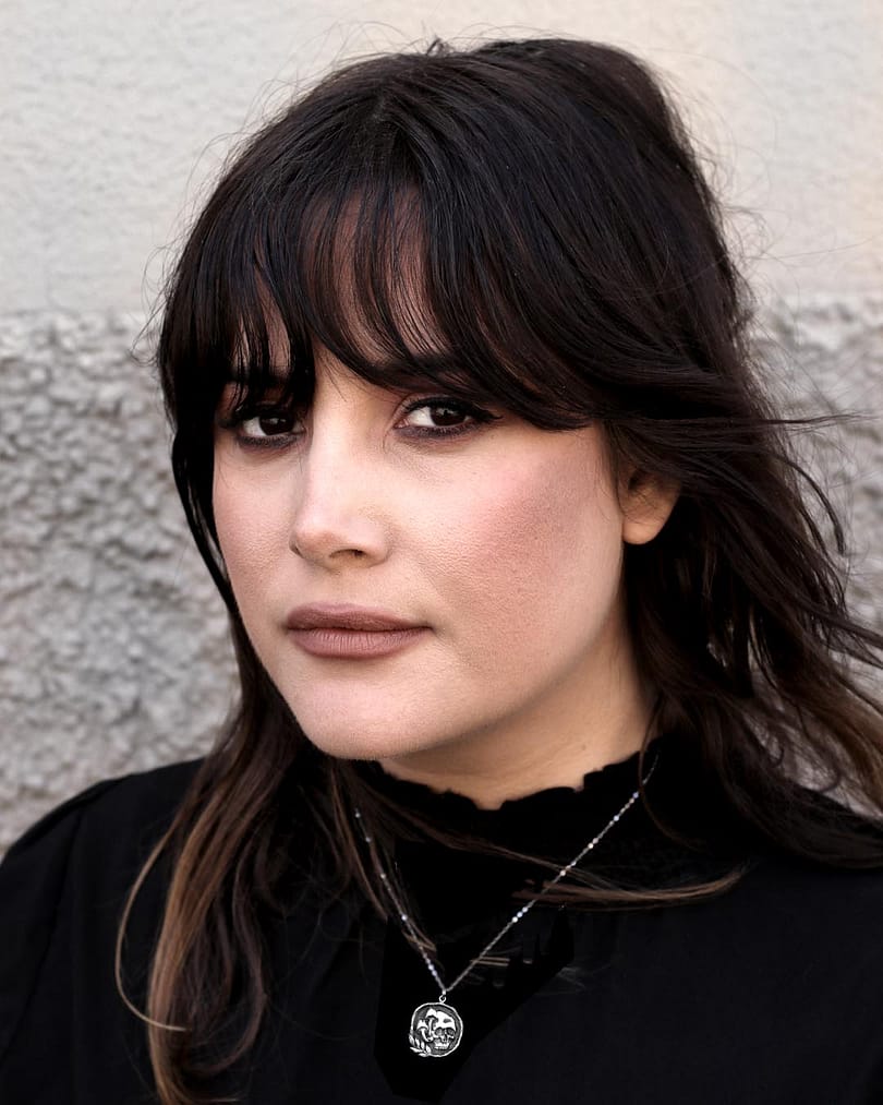 Raven-haired woman wears a recycled sterling silver necklace with intricate details and oxidised finish, the necklace is a skull with mushrooms on its side, enframed with a branch with leaves at the bottom