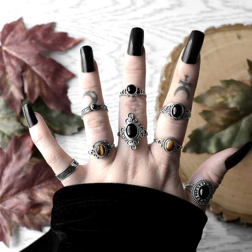 Autumnal ring como, with a large black stone ring, paired with smaller black stone rings and 2 golden brown tiger eye rings, wooden branch and autumn leaves in the background