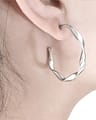 A twisted stainless steel earring hanging in a womans ear.